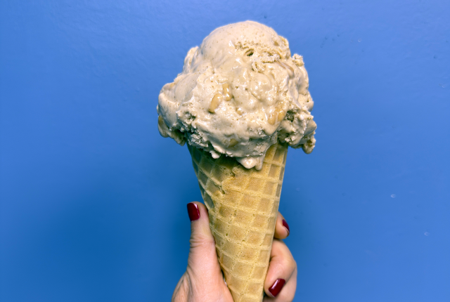 Hand holding an ice cream cone against a blue wall.