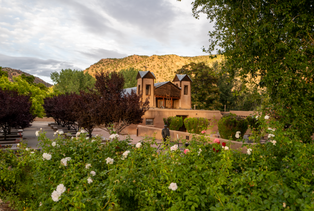 A tranquil courtyard garden with blooming roses welcomes visitors to El Santuario de Chimayó.