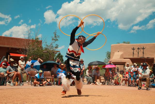 A dancer performs a traditional hoop dance with three hoops in the air, dressed in cultural attire.