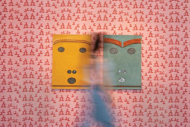 Two abstract face-like artworks on a patterned wall, with a blurred figure walking in front.