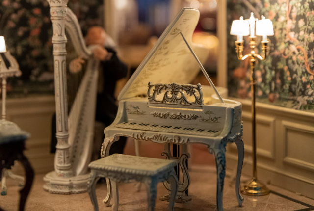A miniature room with a harp, piano, chairs, and chandelier on display at the Miniatures & Curious Collections Museum.