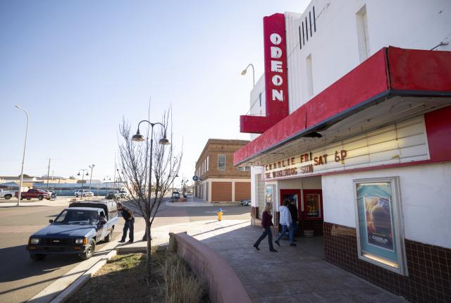 Street view of the Odeon theater with a red sign, people entering, and a vintage car parked nearby.