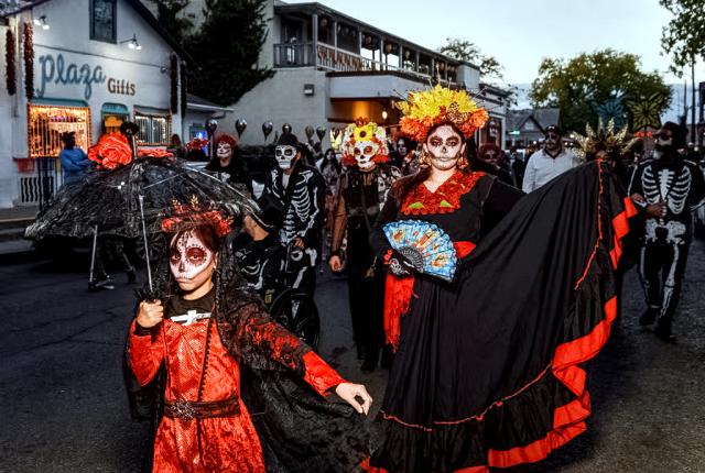 Participants in skeletal face paint and elaborate costumes parade through Old Town Albuquerque.