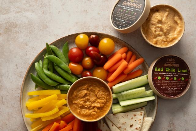 A round tray filled with colorful fresh veggies and two open containers of Taos Sprouted Hummus.