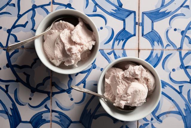 Two white bowls with light pink ice cream and spoons sit on a blue and white patterned tile surface.