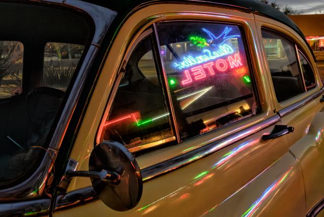 A classic car reflects the neon glow of a motel sign.