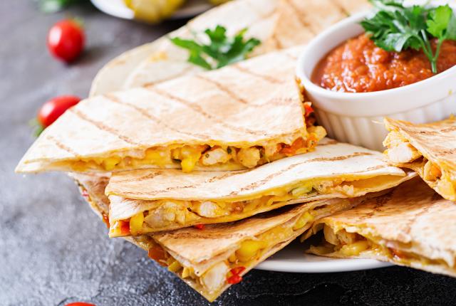 Quesadillas cut in quarters and stacked on a white round plate.