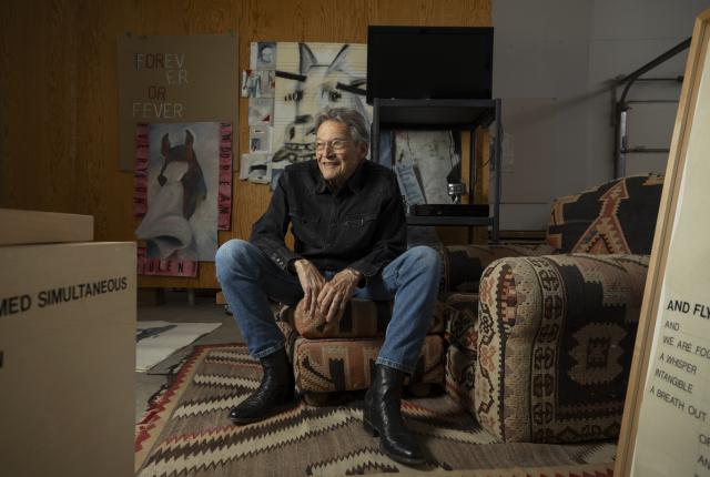 Person sitting in an art studio surrounded by paintings and patterned furniture.