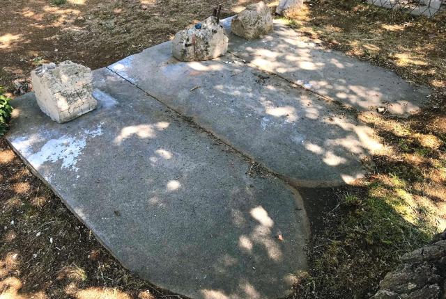 Weathered concrete grave coverings and small stone markers lie beneath dappled tree shade.