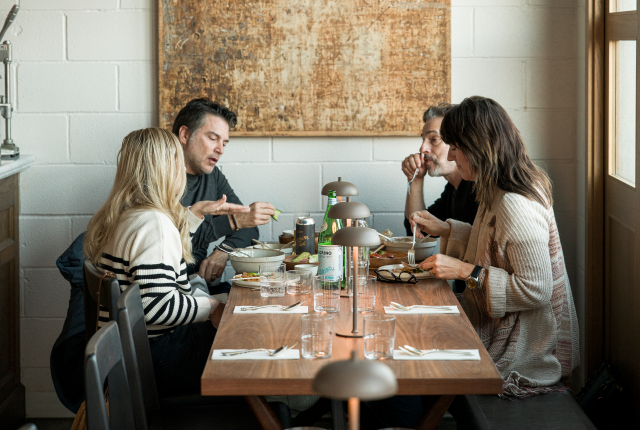 Four people sit around a wooden table in a cozy restaurant, engaged in conversation and eating.