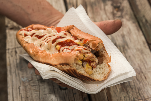 A close-up of a Sonoran-style hot dog wrapped in bacon and nestled into a soft bun, covered with toppings.