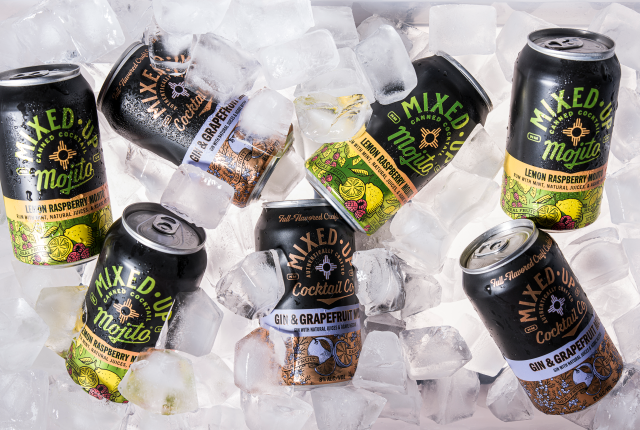Cans of Mixed-Up canned cocktails scattered on ice.