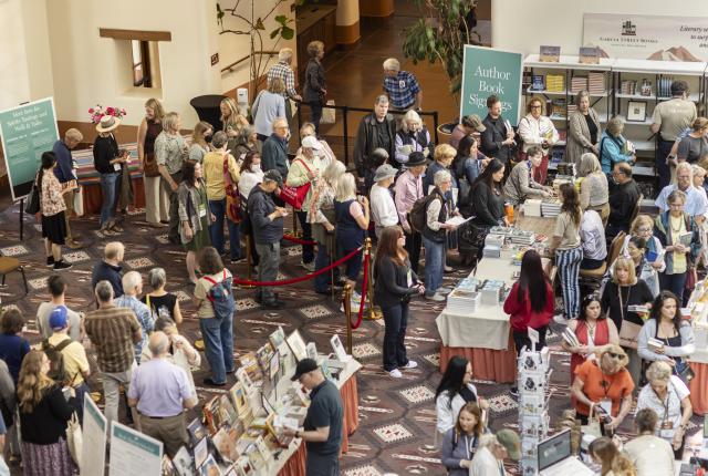 A large group of people attend a the Santa Fe International Literary Festival, gathered around tables with books.