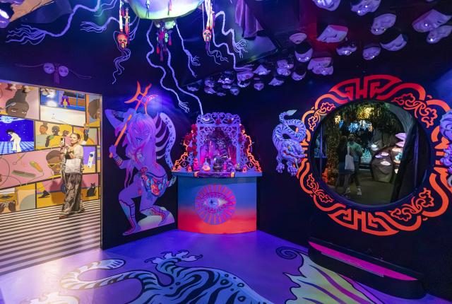 A dark installation room has painted creatures on its walls, a decorate pedestal, and a large circular opening framed in red.