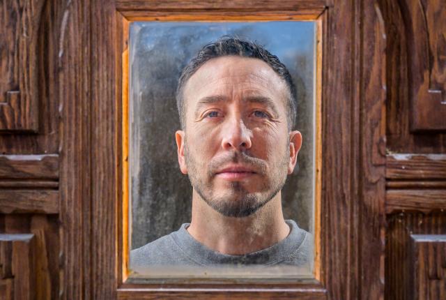 Vicente Telles stares into the mirrored door of his art studio in Albuquerque.