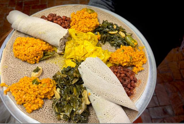 A platter of Ethiopian cuisine featuring various colorful dishes on injera, which is rolled at the edges.