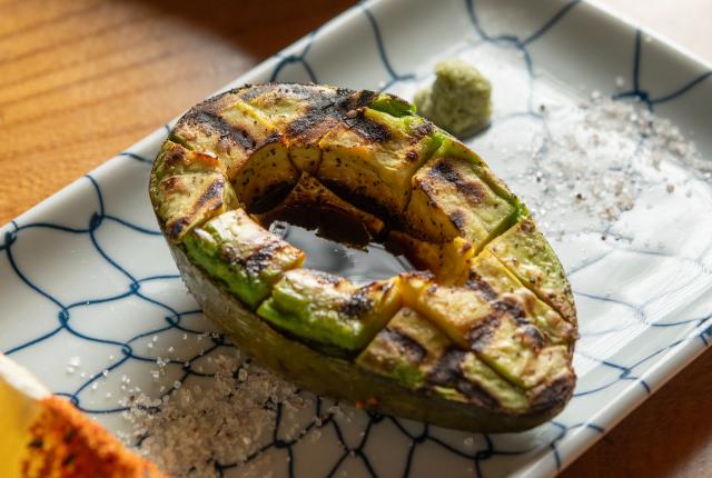 Grilled avocado on a patterned plate with salt and a seasoned lemon wedge.