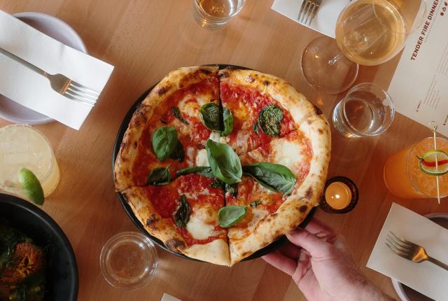 A wood-fired margherita pizza with charred crust, melted mozzarella, and fresh basil leaves.