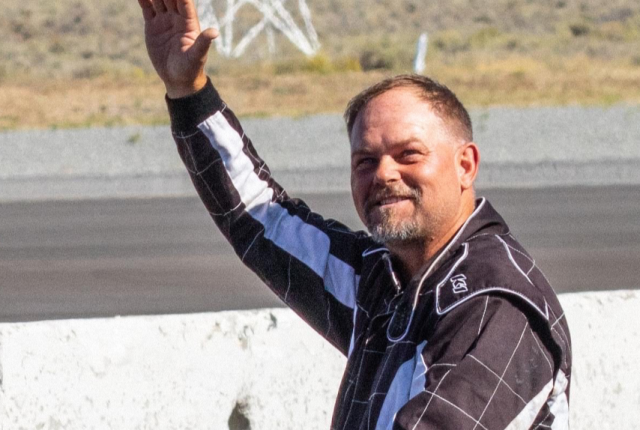 F1 air racing champion Josh Watson waves while wearing a black racing suit.