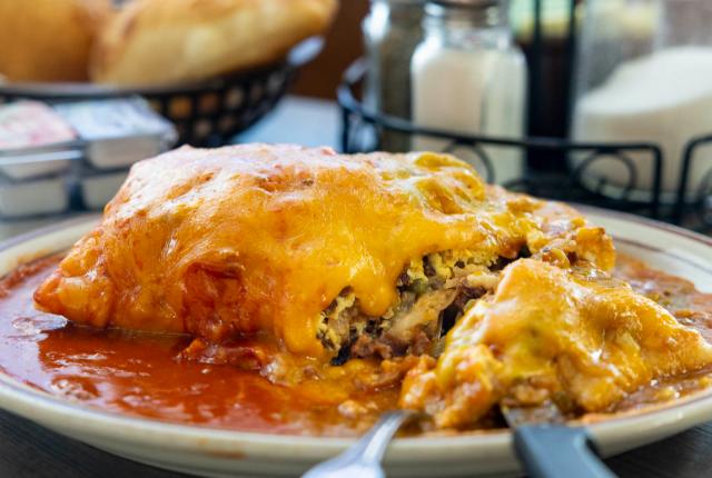 Cheesy enchiladas smothered in red sauce fill a plate with utensils on the side.