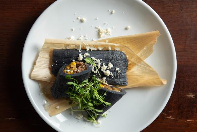 Blue corn rabbit tamales wrapped in husks and topped with colorful garnishes.