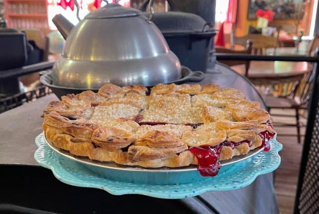Freshly baked berry pie on a blue plate sitting atop a vintage wood stove in a rustic room.