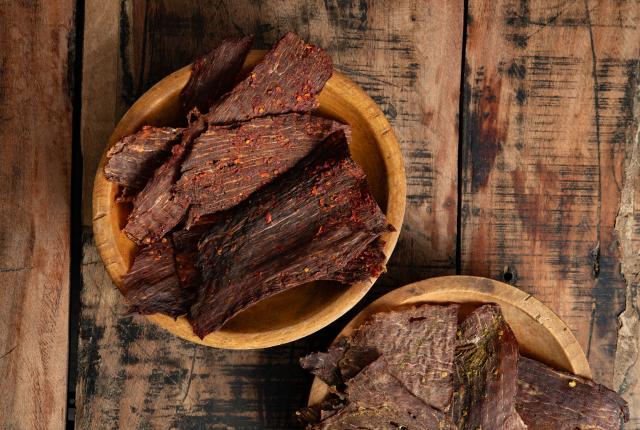 Two wooden bowls filled with seasoned beef jerky on a rustic wooden table.