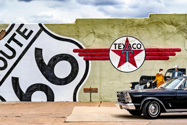 A vintage car parked beside a wall with Route 66 and Texaco logos.