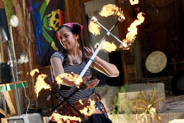 Person performing a fire‑staff routine on an outdoor stage with flames spinning from both ends of the staff.