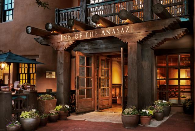 Warm, welcoming hotel entrance with rustic wooden beams and soft lighting, surrounded by potted plants.