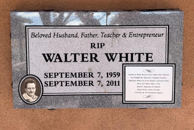 Plaque on a beige wall commemorating Walter White with dates 1959-2011. Includes a small portrait and text reading "Beloved Husband, Father, Teacher & Entrepreneur."