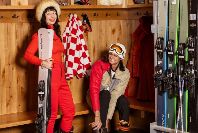 Vanessa Vanya and Alex Vigil gearing up with ski boots and skis inside the Taos Ski Valley locker room.