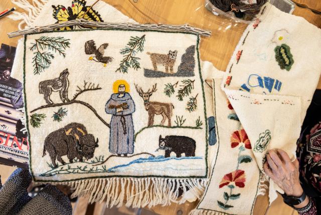 Embroidered textiles on a table featuring animals, plants, and a central figure.
