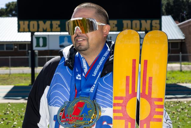 Edward Herrera holds skis with a Zia symbol while wearing racing medals.