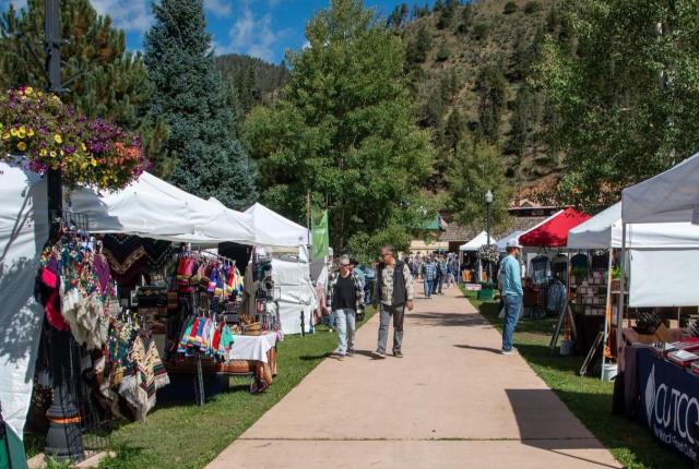 Outdoor market with vendor tents lining a walkway and visitors browsing handmade goods.