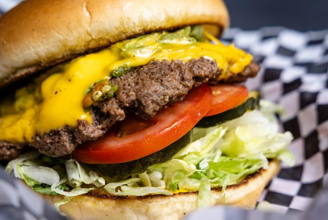 Green chile cheeseburger topped with melted cheddar, lettuce, tomato, and pickles served in a red basket at Isleta Grill along Route 66.