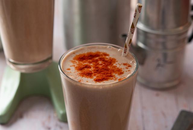 A tall glass filled with a creamy shake, topped with a sprinkle of red spice.