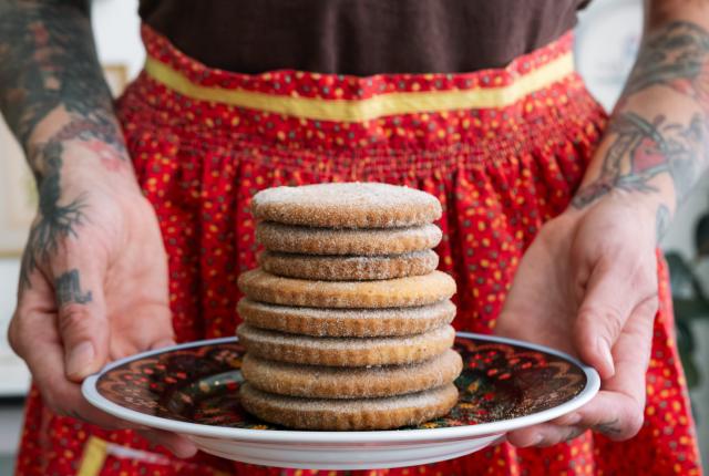 Person holding a plate of stacked cookies while wearing a red apron.
