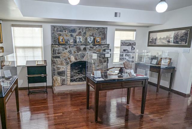 Interior of the Wingfield Heritage House Museum in Ruidoso featuring a large stone fireplaced, framed family photos, and display cases of historical artifacts.