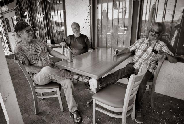Three men gathered outside La Tiendita in Dixon, New Mexico, sharing drinks and conversation as part of the resolana tradition.