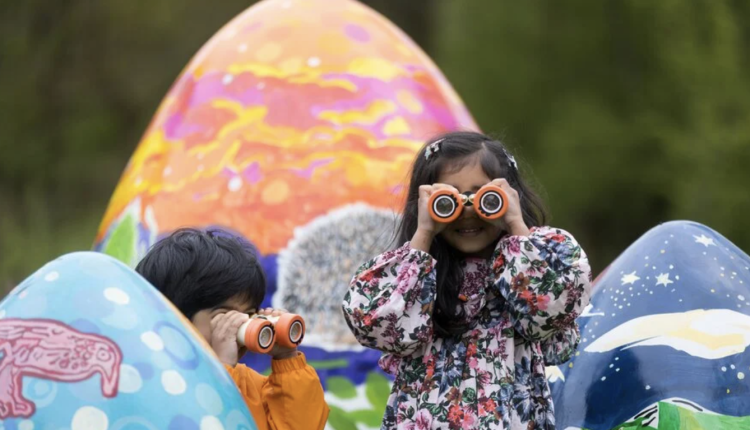 children in puddlesuits looking through binoculars, huge easter eggs in the background