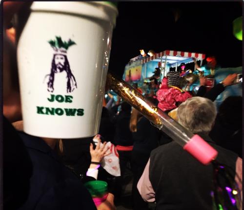 Spectators watch a colorful Mardi Gras float pass near a large “Joe Knows” graphic during the Joe Cain Day parade in Mobile, Alabama.