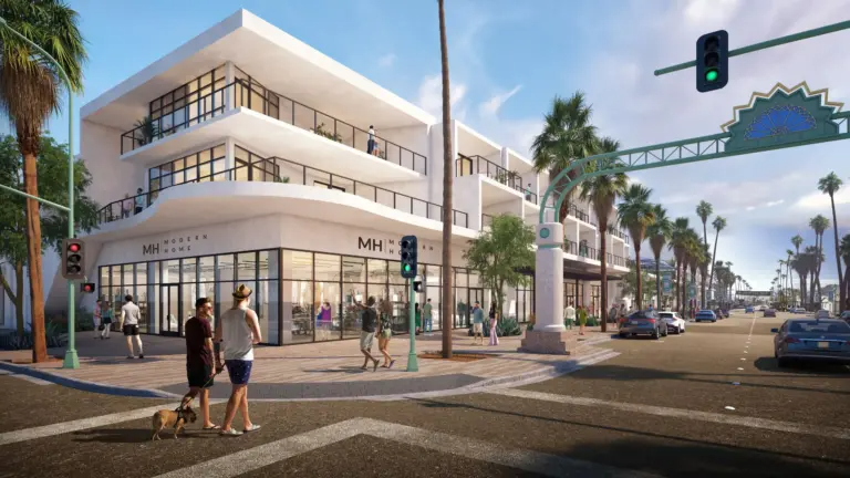 A sunny streetscape with modern two-story white buildings on the left, palm trees lining the road, pedestrians, some with a dog, crossing the street, cars on the road, and a traffic light showing green.