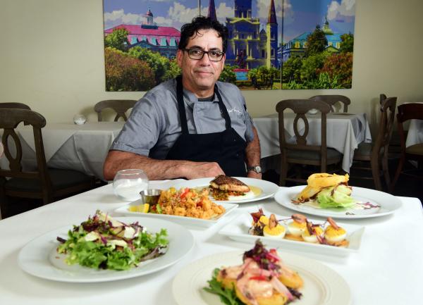 Chef Robert Vasquez, Forks & Corks, sits at a table with various dishes hehas prepared.