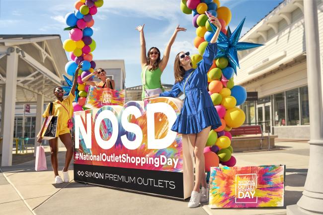 Women standing by a National Outlet Shopping Day sign