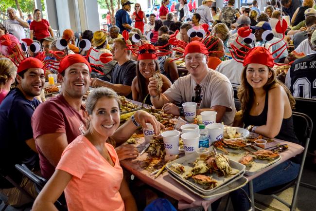 A group of people wearing crab hats sitting around a table picking crabs