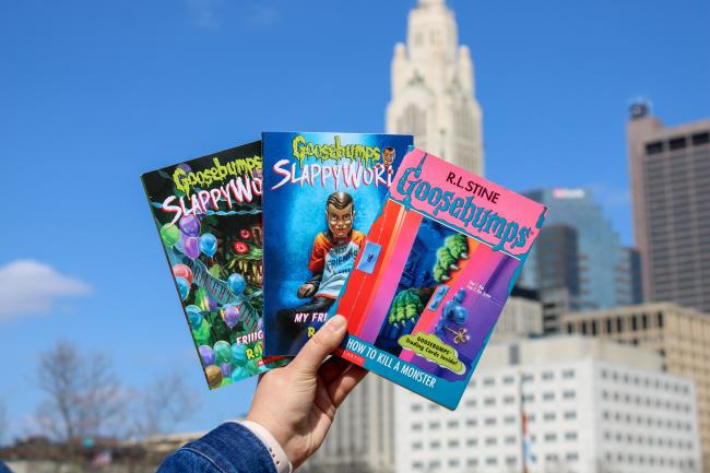 Three Goosebumps books held up against a Columbus skyline