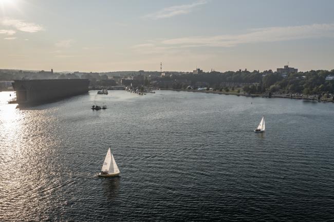 An aerial view of a sailboat at sunset in front of the Ore Dock in Lower Harbor on Lake Superior in Marquette, MI