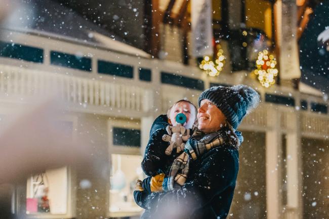 Mom Holding Child, Enjoying the Falling Snow at a Shopping Center