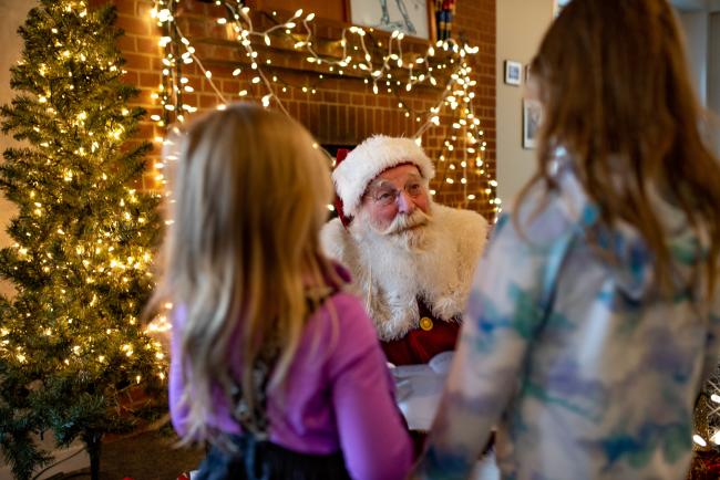 Santa Smiling at Two Girls with Christmas Lights in Background